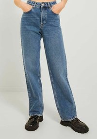 Jeans in denim azzurro chiaro con gamba larga e vita alta, dotati di tasche frontali, passanti per cintura e una leggera texture sbiadita. Abbinati a scarpe con plateau nere e chunky.