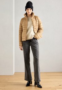 Beige dunjakke, lynlås lukning, med horisontalt quiltet mønster. Sammen med en cremefarvet sweater, grå flared jeans og sorte hælede ankelstøvler.