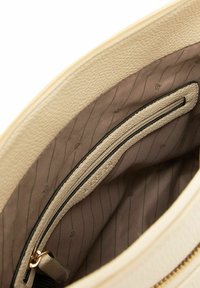 Interno della borsa beige strutturato con fodera testurizzata, dotato di una tasca con zip e una finitura liscia. Sottile motivo a righe orizzontali.