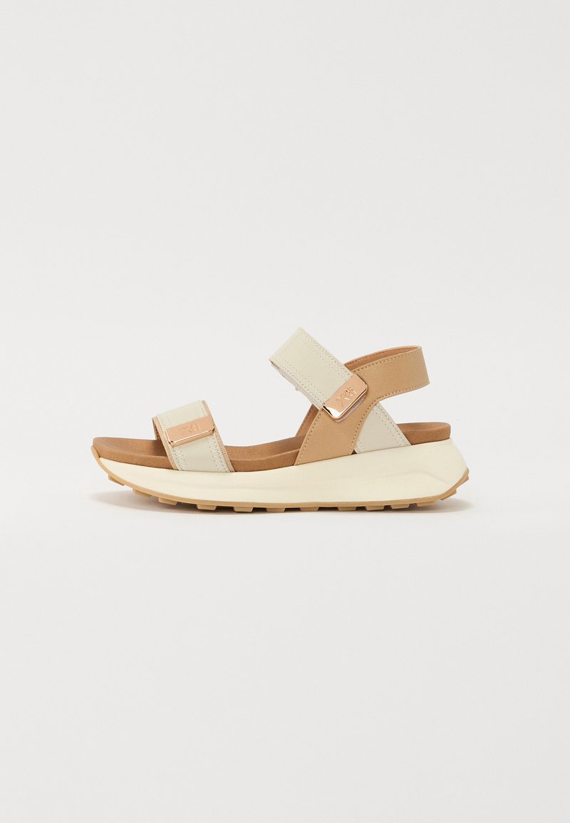 Brune og kremfargede sandaler med justerbare stropper, myk fotseng og teksturert gummisåle. Metalliske detaljer gir tillegg til designet.