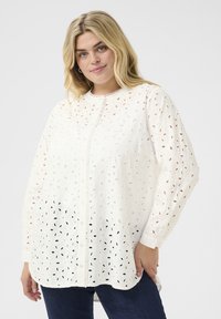 Blusa blanca de botones confeccionada con tejido bordado que presenta detalles de ojales, mangas largas y un escote redondo. El dobladillo es ligeramente curvado.