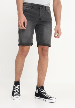 Person iført optrukne sorte denimshorts kombineret med sorte høje canvas-sneakers med hvide snørebånd og såler.