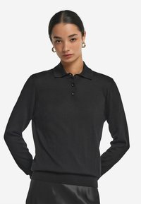 Czarny sweter polo z długim rękawem, wykonany z teksturowanej tkaniny, z zapięciem na guziki oraz ściągaczami przy mankietach i u dołu. Gładki, minimalistyczny design.