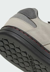 Grey suede shoe with textured fabric accents, black rubber sole featuring circular tread pattern, red stitching along the edge.