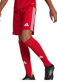 Rode voetbalshorts met drie witte strepen aan de zijkanten, gecombineerd met rode knie-hoge sokken met witte accenten, en zwarte voetbalschoenen.