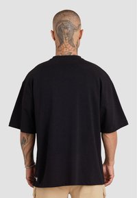 Zwart katoenen t-shirt met een losse pasvorm, brede mouwen en een klein logo aan de zoom. Heeft een grote slangentattoo op de achterkant van de nek.
