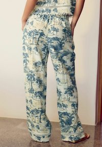 Pantaloni a gamba larga in tessuto leggero caratterizzati da una stampa paesaggistica blu e beige. Accentuati da un bordo decorativo all'orlo.