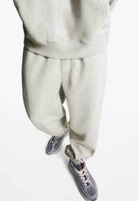 Light gray sweatpants with a relaxed fit, elastic cuffs, and matching sweatshirt. Paired with gray sneakers featuring mesh and rubber accents.