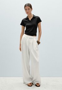 Black short-sleeve polo shirt, white wide-leg trousers, brown bracelet, and black flip-flops with red accents. Plain background.