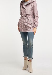 Veste waterproof rose clair avec une taille cintrée, capuche avec cordon de serrage et poches zippées, assortie à un jean bleu retroussé et des bottines beiges.