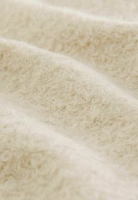 Mäkká, textúrovaná látka vo svetlej smotanovej farbe, s jemnými vláknami vytvárajúcimi teplý vzhľad. Materiál pôsobí ľahko a nadýchane.