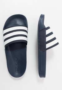 Blauwe slide-sandalen met drie witte parallelle strepen en een gestructureerde bovenkant. Bevat een gewatteerde voetbed en een reliëflogo op de zool.