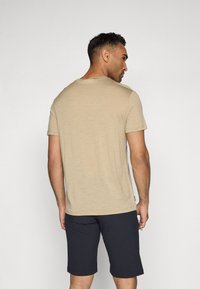 Camiseta de manga corta beige con cuello redondo, hecha de una tela suave y texturizada, combinada con pantalones cortos azul marino oscuro, vista desde atrás.