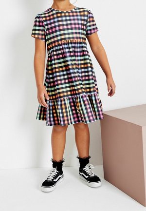 Robe à carreaux multicolores avec des manches courtes et un ourlet à volants, fabriquée en tissu léger. Assortie à des baskets noires et des chaussettes à volants.