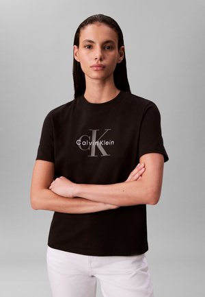 Μαύρο βαμβακερό κοντομάνικο t-shirt με γκρι λογότυπο "Calvin Klein" και εμφανές έμβλημα "CK" στο κέντρο. Απλός, καθημερινός σχεδιασμός.