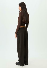Brun langærmet top og sorte vide bukser med en glat tekstur og en afslappet pasform. Sorte sko fuldender outfittet.