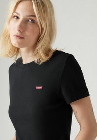 Mustat lyhyet hiha t-paita, joka on valmistettu puuvillasta ja jossa on pieni punainen Levi's-logopatchi vasemmassa rinnassa. Taipeellinen tekstuuri ja istuva muotoilu.