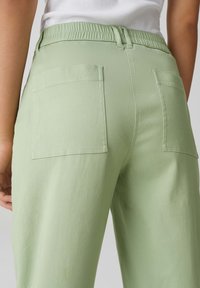 Pantalons larges vert clair avec une ceinture élastique, comportant deux poches arrière et une texture lisse et mate.