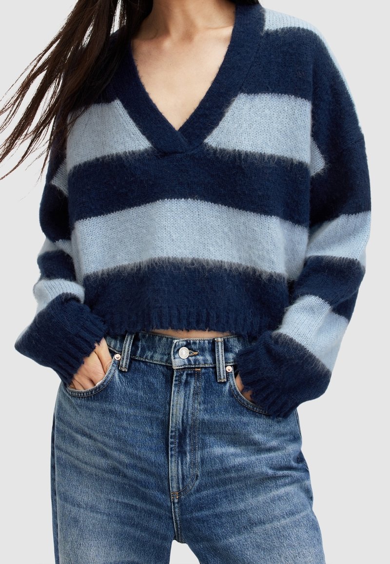 Sweter w jasnoniebiesko-granatowe paski, wykonany na drutach, z głębokim dekoltem w serek i krótkim fasonem. Posiada prążkowane mankiety i dół. Połączony z jeansami z wysokim stanem.
