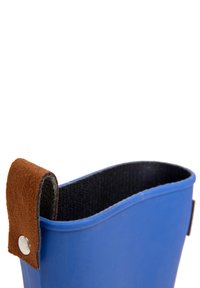 Blauer Gummistiefel mit einem braunen Wildledergurt und schwarer Innenauskleidung. Der obere Rand ist gewellt und schafft eine geschwungene Silhouette.
