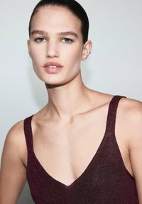 Burgundy sleeveless top with a deep V-neckline, featuring a textured fabric that catches light, highlighting its shimmering details.