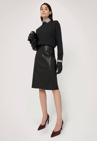 Černý svetr z dánského úpletu v kombinaci s lesklou černou koženou sukní, černými rukavicemi a bordó lodičkami s špičatou špičkou. Viditelný proužkovaný límec.