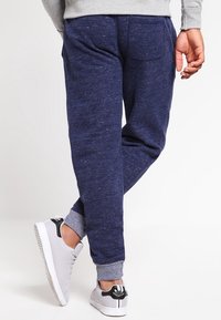 Marineblaue Jogginghosen mit weicher Textur, verjüngten Knöcheln, elastischem Bund und einer Gesäßtasche, kombiniert mit weißen Mesh-Sneakers.