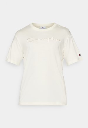 Krémové bavlnené tričko s krátkymi rukávmi, na prednej strane s vyšitým logom "Champion" a látkovou nášivkou na ľavom rukáve.