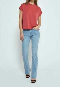 Haut court couleur rouille associé à un jean évasé bleu clair et des escarpins noirs ouverts. Le haut a un col rond et une coupe décontractée.