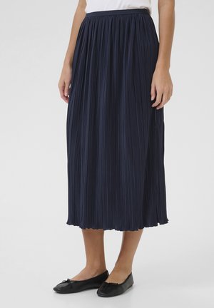 Marineblauwe geplooide midi rok met een zachte textuur, elastische tailleband en een gerimpelde zoom, gecombineerd met zwarte platte schoenen.