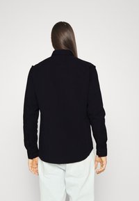 Zwarte shirt met knoopsluiting en lange mouwen, voorzien van een klassieke kraag en een gebogen zoom. Ontworpen in een effen kleur zonder zichtbare patronen.