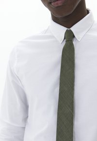 Cravate verte texturée au design slim, portée sur une chemise blanche à col pointu avec des boutons visibles. Apparence simple et élégante.