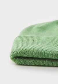 Groene gebreide beanie met een geribbelde manchet. Zachte textuur met een omgevouwen rand, die een effen kleur laat zien zonder patronen of versieringen.