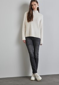 Gruby biały sweter z wysokim kołnierzem i ściągaczami, w połączeniu z ciemnoszarymi obcisłymi dżinsami i białymi sneakersami. Gładka faktura, swobodny design.