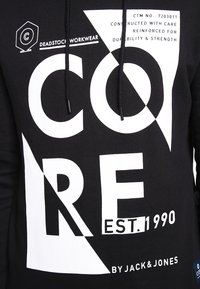 Sudadera negra con capucha que presenta un atrevido texto blanco y elementos gráficos, con cordones y una etiqueta de logo en la parte inferior izquierda. Diseñada para durabilidad.