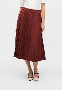 Μπορντό πλισέ φούστα από μαλακό ύφασμα, με ψηλή μέση και ρέουσα σιλουέτα, σε συνδυασμό με δίχρωμα παπούτσια με μαύρες λεπτομέρειες.