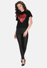 Sort t-shirt med et stort rødt glitrende hjerte og teksten "love", parret med sorte skinny bukser og højhælede sko. Glat stof, afslappet design.