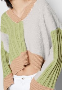 Gebreid cropped sweater in groen, beige en grijs, met een V-hals, geribbelde manchetten en een textured stof met een mix van patronen.
