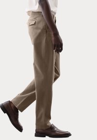Pantalones de algodón beige con un ajuste entallado, bolsillos laterales y un bolsillo trasero único, combinados con mocasines de cuero marrón.