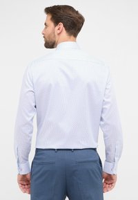 Camicia azzurra a maniche lunghe con un piccolo motivo a pois, dotata di colletto classico e polsini abbottonati, indossata con pantaloni blu scuro.