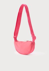 Różowa nylonowa torebka na ramię o zaokrąglonym kształcie, wyposażona w zamek błyskawiczny i regulowany pasek z tłoczonym logo marki. Lekka konstrukcja.