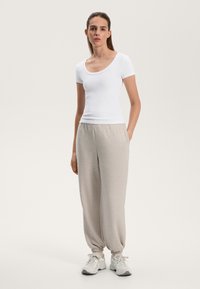 Bílý přiléhavý tričko s kulatým výstřihem v kombinaci s světle šedými zúženými tepláky. Kalhoty mají elastické manžety a boční kapsy. Na nohou jsou tenisky.