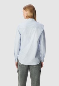 Camicia a maniche lunghe a righe blu chiaro e bianche con taglio dritto, colletto a bottoni e fondo arrotondato, realizzata in tessuto di cotone.