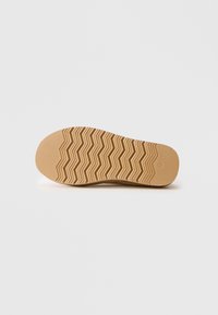 Semelle d'une chaussure beige avec un motif de semelle en zigzag et à pois, taille marquée comme 37, sur un fond clair.