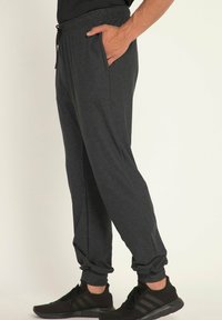 Grijze sportieve joggers met een trekkoord in de taille, zijzakken, taps toelopende boorden en een zachte, gestructureerde stof. Draag met zwarte sportschoenen.