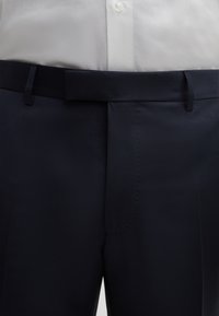 Pantaloni blu navy realizzati in un tessuto liscio, con un design dritto, una cintura e dettagli di cucitura discreti.