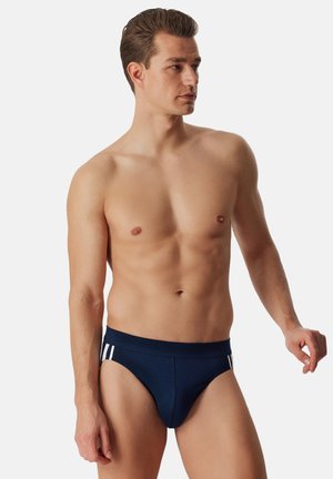 Marineblaue Badehose mit weißen Streifendetails, aus elastischem Stoff gefertigt. Verfügt über ein eng anliegendes Design mit einem breiten Bund.