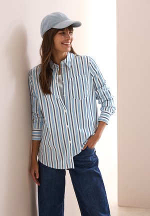Light blue and white striped button-up shirt with a single pocket, paired with dark blue wide-leg jeans and a matching light blue cap.
