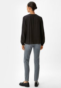 Schwarze Bluse mit langen Ärmeln und gerafften Manschetten, kombiniert mit taillierten grauen Jeans und schwarzen Slippern. Glattes Material und lockere Passform.