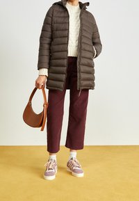Veste rembourrée marron avec capuche, pull en tricot crème, pantalon court en velours côtelé bordeaux et baskets roses. Un sac à main marron complète la tenue.